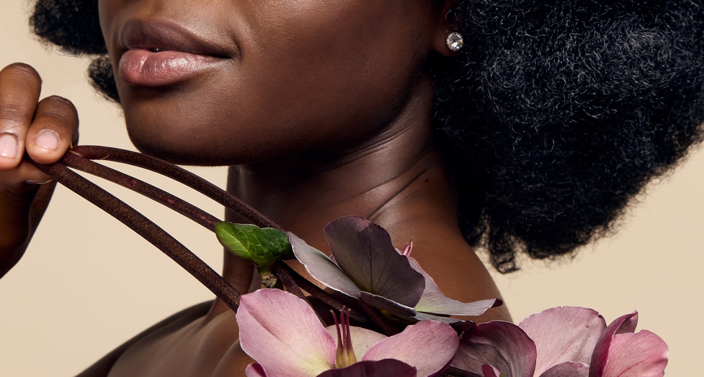 A model with black skin showcasing their glowing, radiant complexion achieved with James Read's Self Glow tanning products while holding a flower, emphasising the natural beauty of the results.