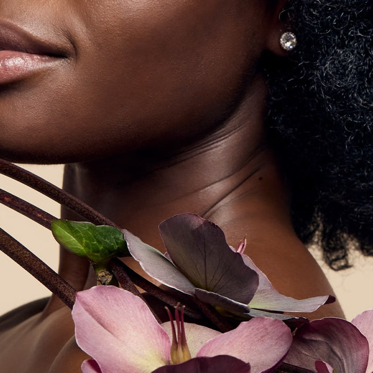 A model with black skin showcasing their glowing, radiant complexion achieved with James Read's Self Glow tanning products while holding a flower, emphasising the natural beauty of the results.