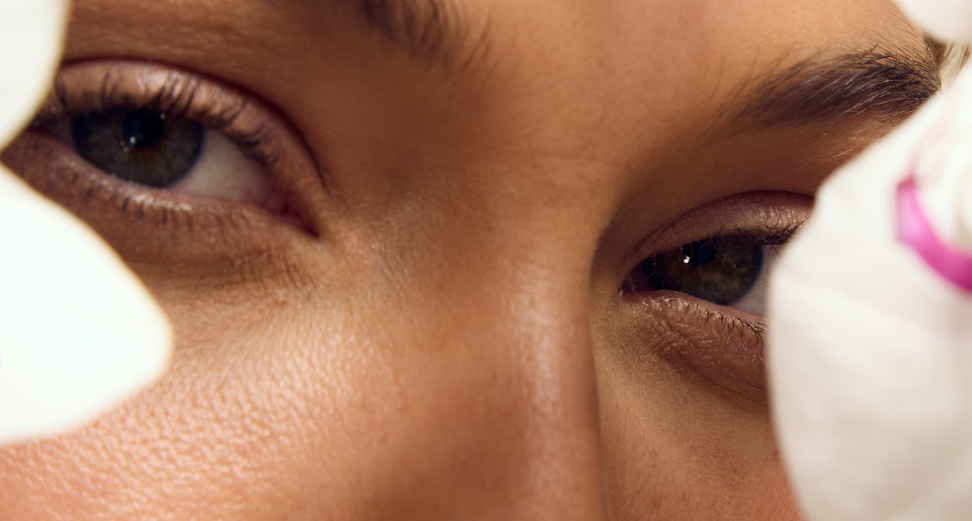 A close-up of a model looking through flowers at the camera, emphasizing Self Glow by James Read's commitment to using sustainable packaging and ingredients in their sunless tanning products, promoting natural beauty and environmental responsibility.