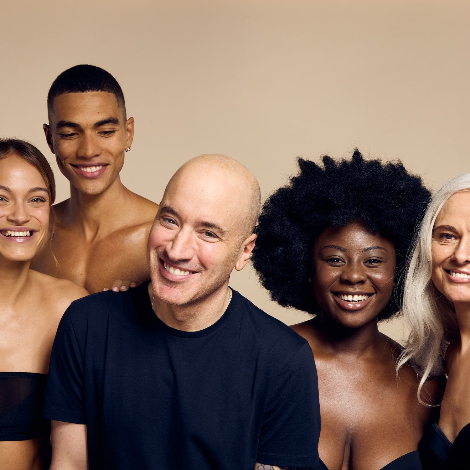 James Read, founder of Self Glow and celebrity spray tan artist, smiling with a diverse group of models showcasing various skin tones and types, highlighting the brand's commitment to inclusivity and delivering natural-looking glowing results for all.