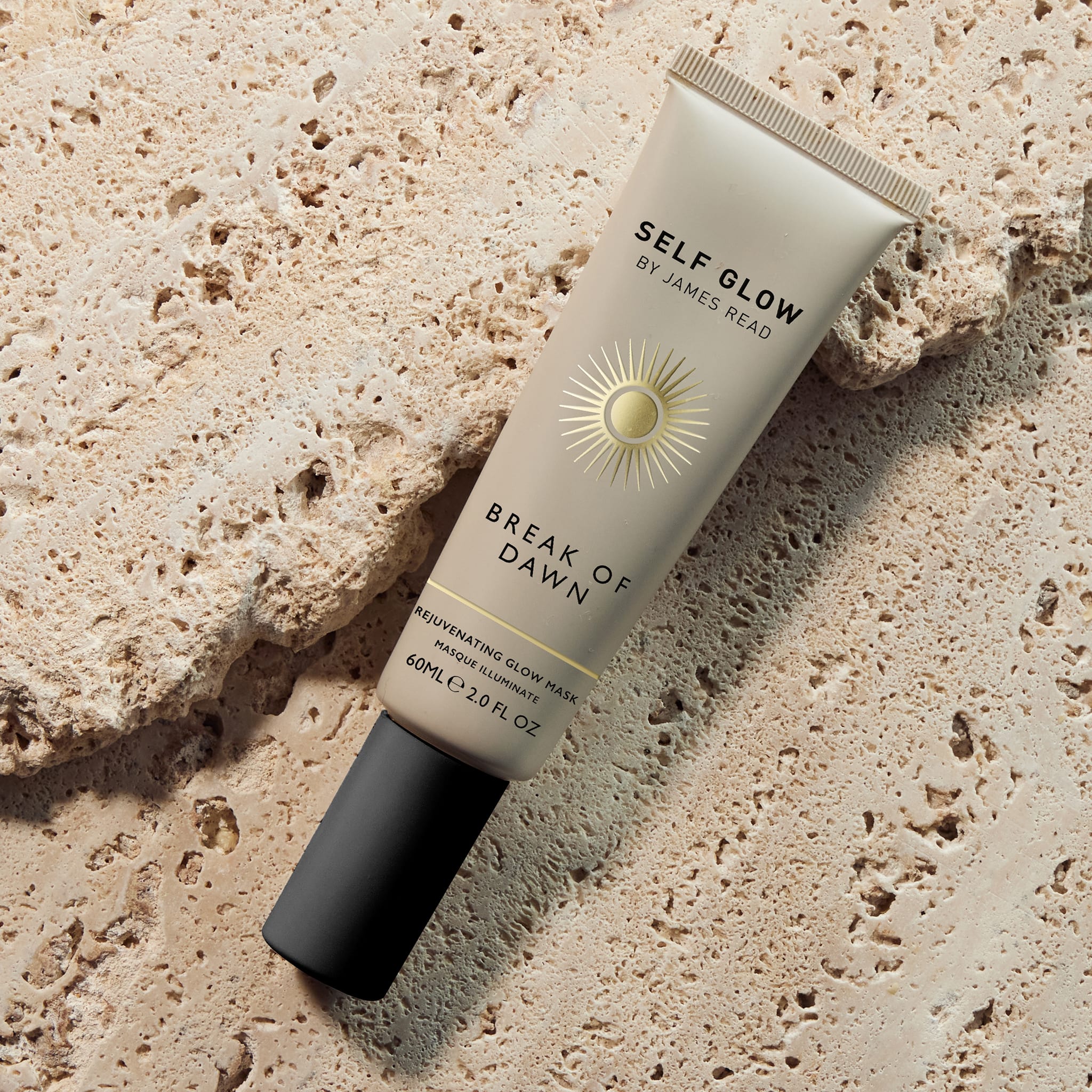 Self Glow by James Read Break of Dawn Rejuvenating Glow Mask bottle in a lifestyle image against rocks in a natural setting, showcasing the 20-minute pre-makeup glow mask for a natural-looking fake tan.