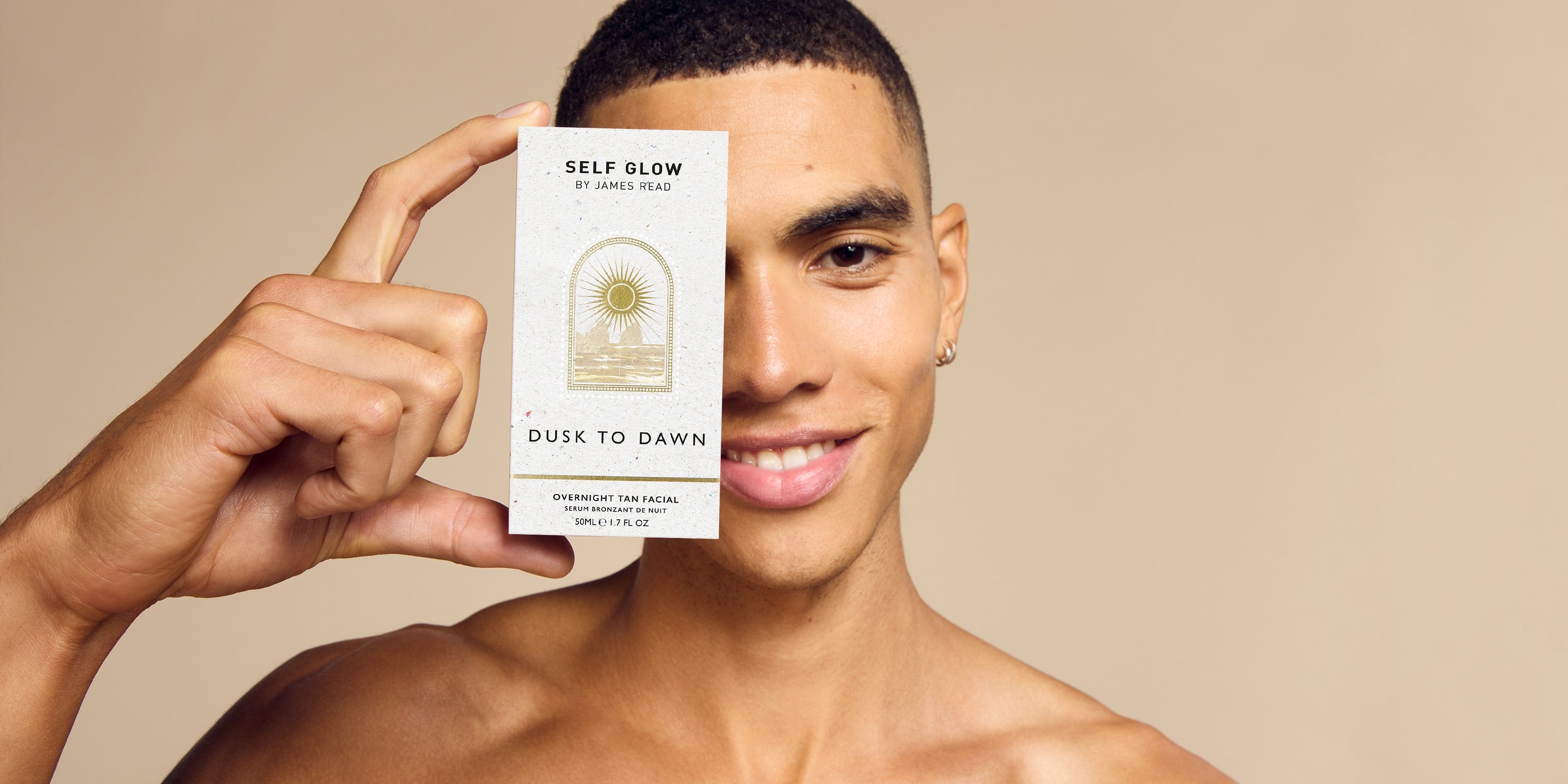 A smiling male model holding the Self Glow by James Read Dusk to Dawn Overnight Tan Facial product box up to his eye, positioned next to the "Why We Love It" text.