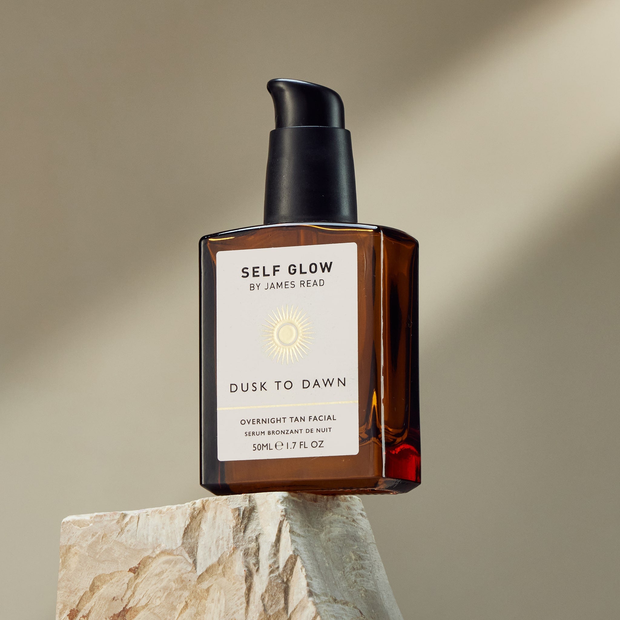 A lifestyle shot of Self Glow by James Read Dusk to Dawn Overnight Tan Facial placed on a rock with the sun shining down, highlighting the product's ability to deliver a natural-looking, sun-kissed glow.