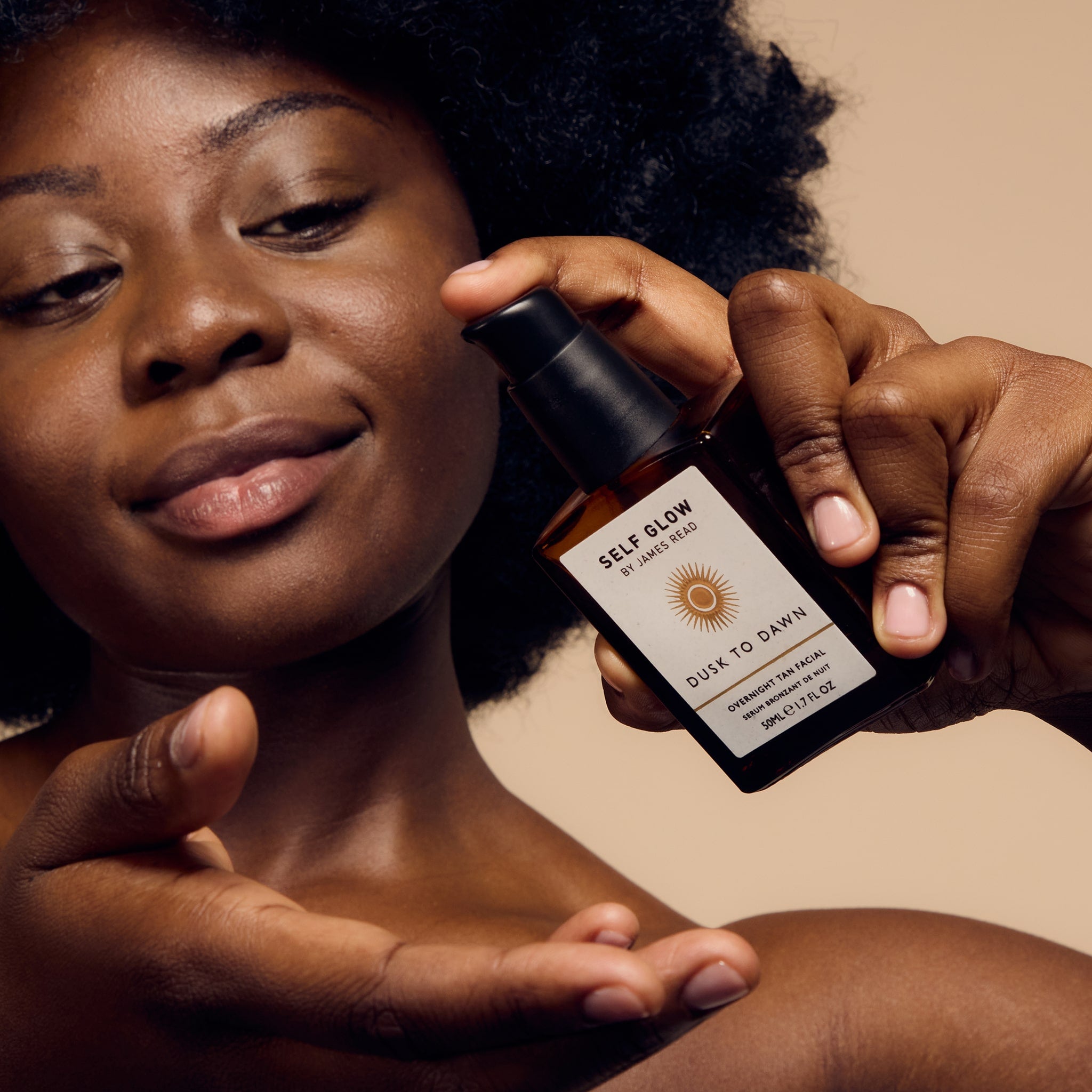 A black woman applying Self Glow by James Read Dusk to Dawn Overnight Tan Facial to her hand, showcasing the product's suitability for all skin types and tones.