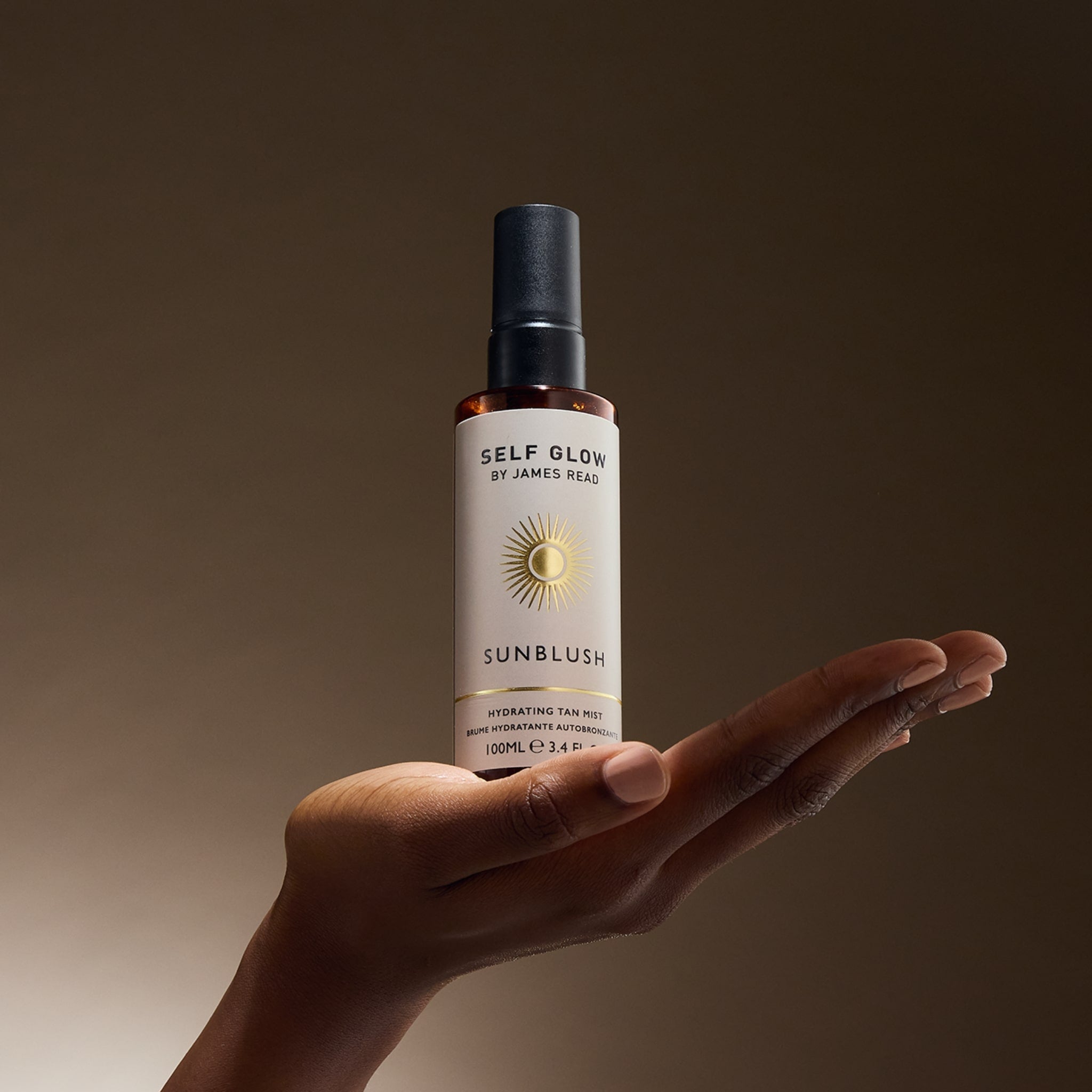 Image of a woman's hand balancing the Self Glow by James Read product Sunblush Hydrating Tan Mist with a warm skin tone background.