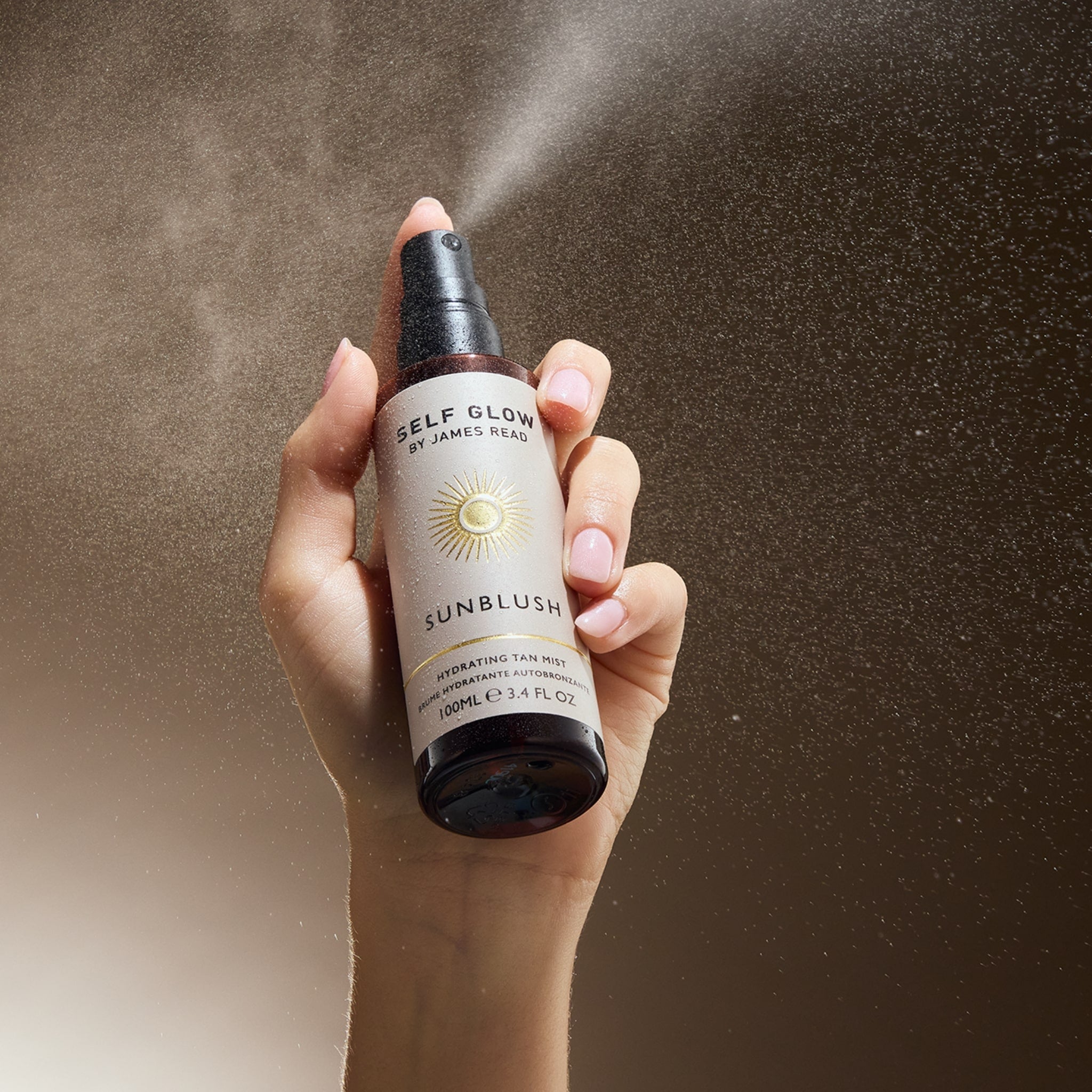 Image of a woman's hand spraying the Self Glow by James Read product Sunblush Hydrating Tan Mist with a warm skin tone background.