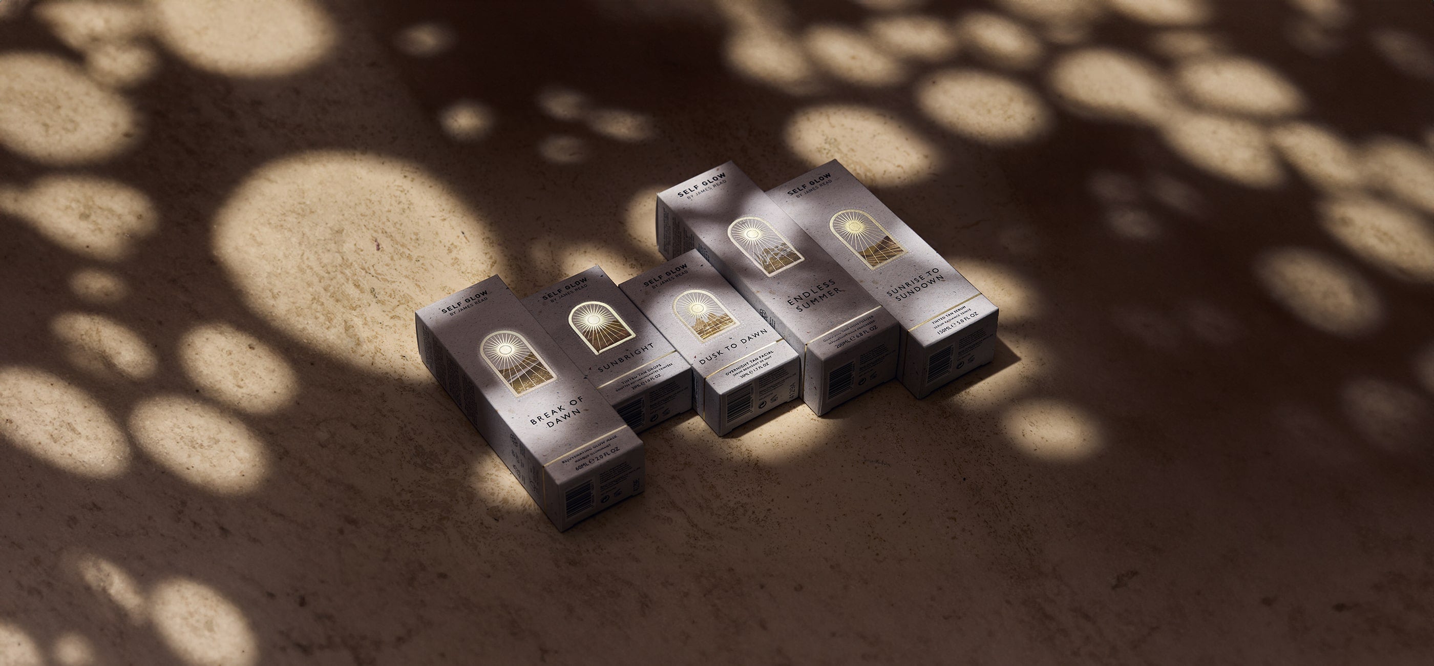 James Read Self Glow sunless tanning skincare product range in a lifestyle image with golden light, featuring product boxes for a luxurious fake tan experience.
